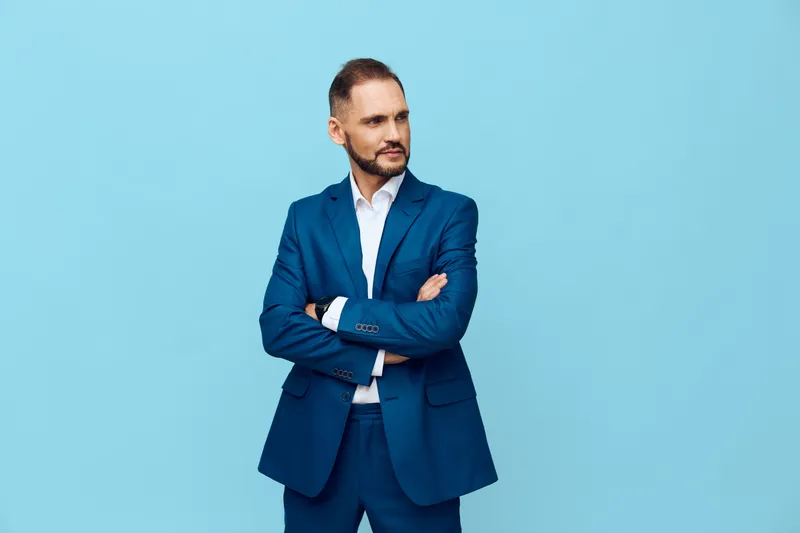 Professional businessman stands with arms crossed on a vivid blue background, projecting confidence, focus, and poised leadership in a modern work scene. A strong, clear pose conveys executive