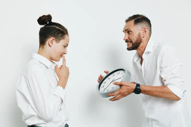 A professional businessman stands with a calm, focused expression as he discusses timing with a colleague against a solid white background.