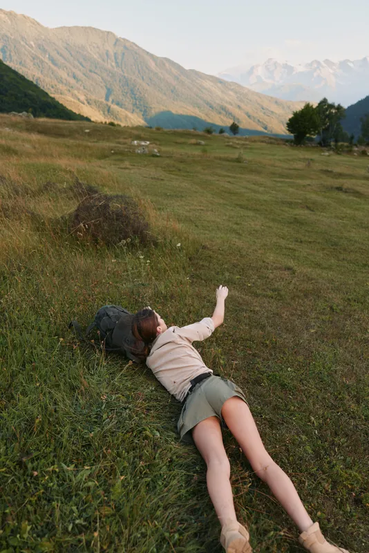 Woman lying on grass in a mountain valley, outdoor landscape, lifestyle moment of rest, exploration and calm in warm natural light, Calm, wide valley view.