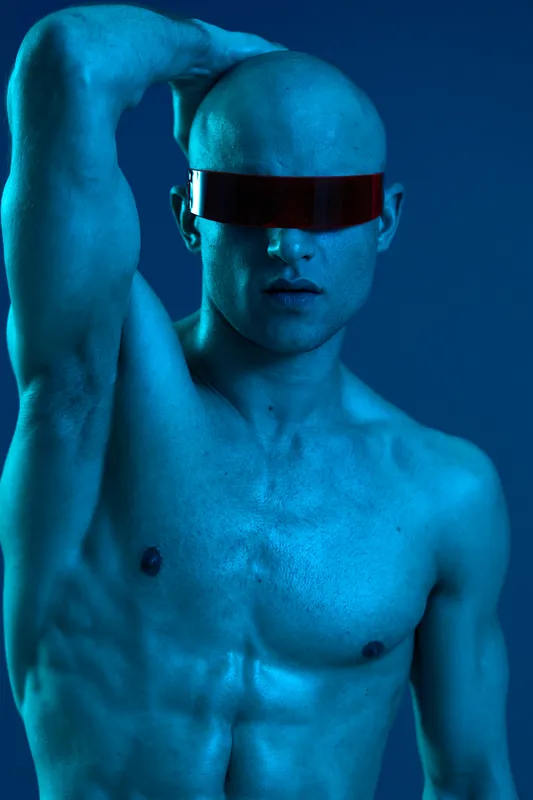 Strong man posing with futuristic sunglasses, showcasing a striking blue hue, emphasizing confidence and charisma in a modern setting.