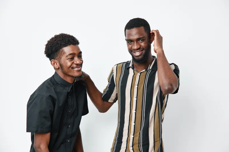 Two young black men with dark skin smiling and interacting in casual clothing on white background. Friendship, happiness and positive emotions between african american males in studio.