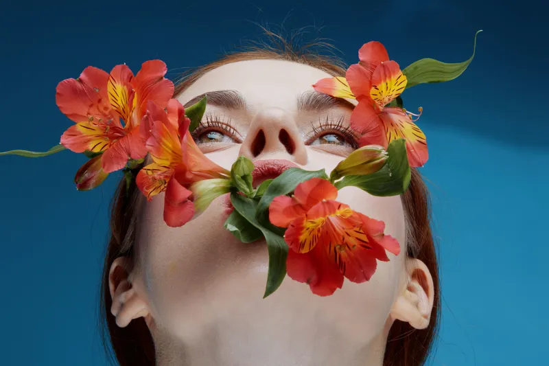 A captivating portrait of a woman with red flowers, symbolizing beauty and nature, against a vibrant blue background, expressing serenity and creativity