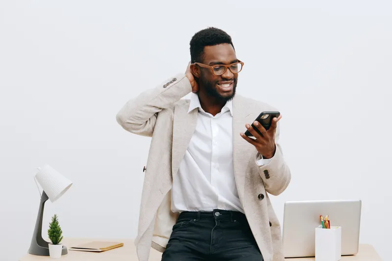 Smiling man with glasses holding smartphone in hand, standing in bright modern office with minimal decor, working on new project, happy mood, casual smart outfit, white background, technology concept,