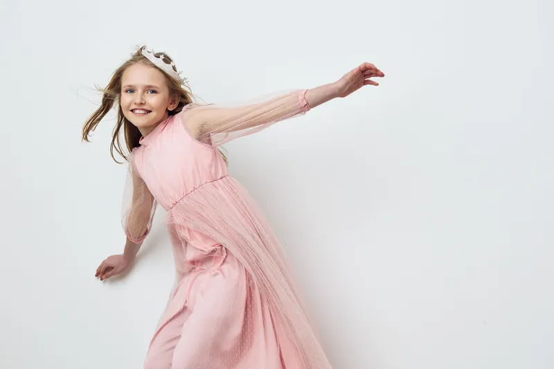Joyful girl in a pink dress dancing against a light background, expressing happiness and freedom, ideal for children s fashion and spring themes