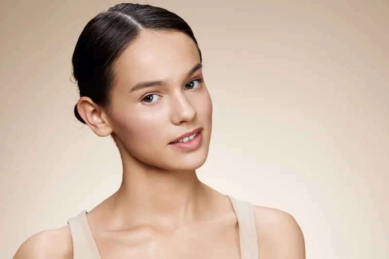 Portrait of a young woman with smooth skin, wearing a beige top, showcasing a confident expression against a soft neutral background Natural beauty, skincare, and self care focus