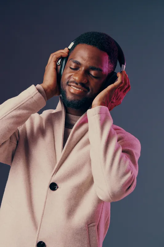 A stylish young man enjoying music, wearing headphones, with a joyful expression in a modern, softly lit background