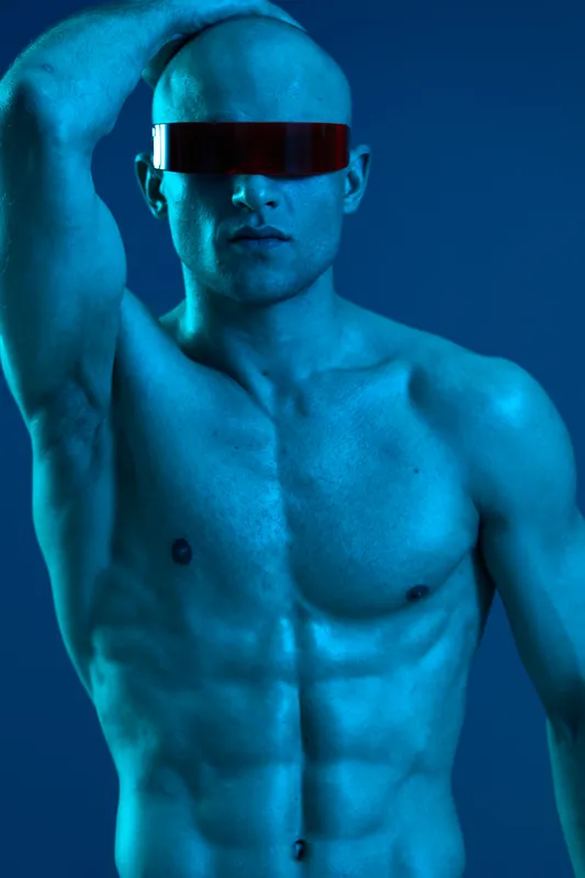 Athletic man with sunglasses striking a confident pose against a blue background. The photo emphasizes a modern, artistic style that draws attention.