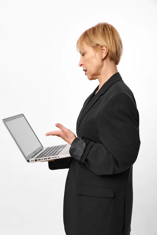 Woman using laptop in business suit, profile view. Hands gesturing while typing, showing stress and communication in office work. Isolated on white background.