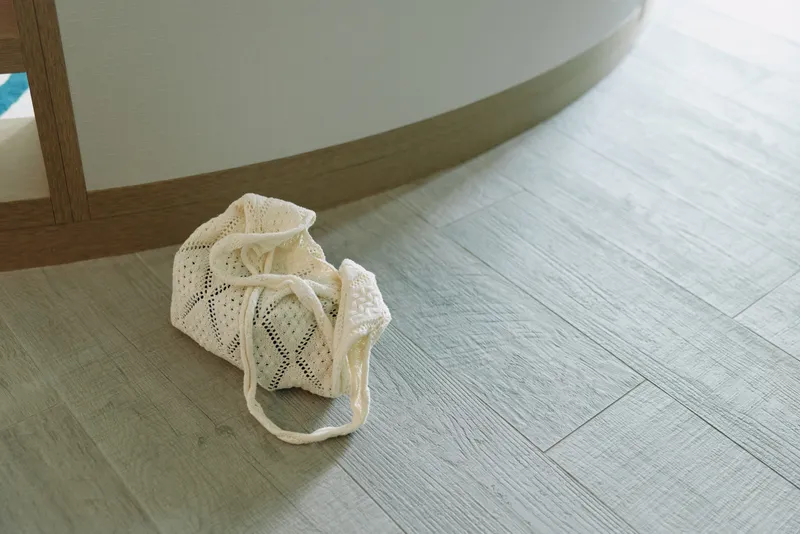 Handmade baby booties on a light wooden floor beside curved furniture, delicate textile footwear for infants, soft yarn textures and cozy charm in a calm home setting.
