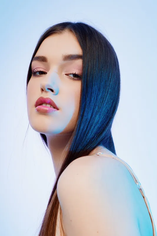 Young woman with long dark hair poses with a confident expression in soft studio lighting. Concept of beauty, fashion, and elegance with a smooth skin tone and makeup.