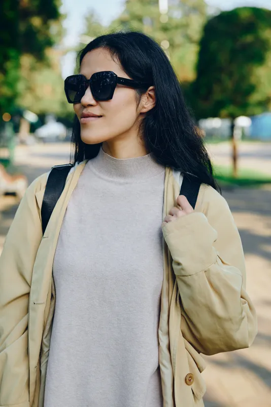 Sunglasses, woman, outdoor fashion in a beige coat and gray sweater, park setting with sunlight, casual style and relaxed mood, urban leisure vibe