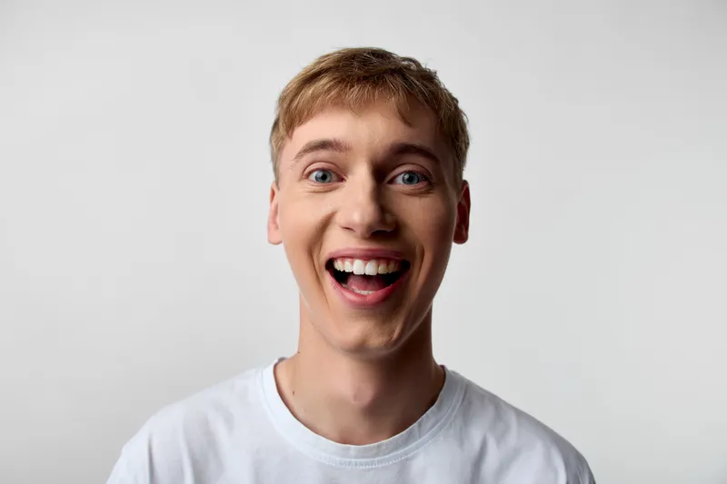 Bright closeup of a smiling man in a white tshirt, radiating happiness and friendly energy, suitable for lifestyle, branding, and positivity campaigns in a clean studio with soft lighting for