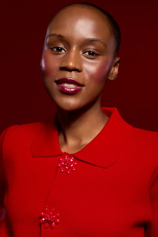 Portrait of a confident black woman with dark skin wearing a red sweater with decorative buttons on a red background. Concept of beauty, fashion, and elegance with vibrant colors.