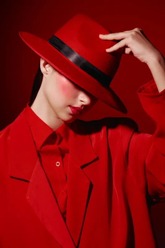 Stylish young woman wearing a red hat and red coat poses fashionably against a red background. Bold makeup and monochrome look create an artistic beauty concept.