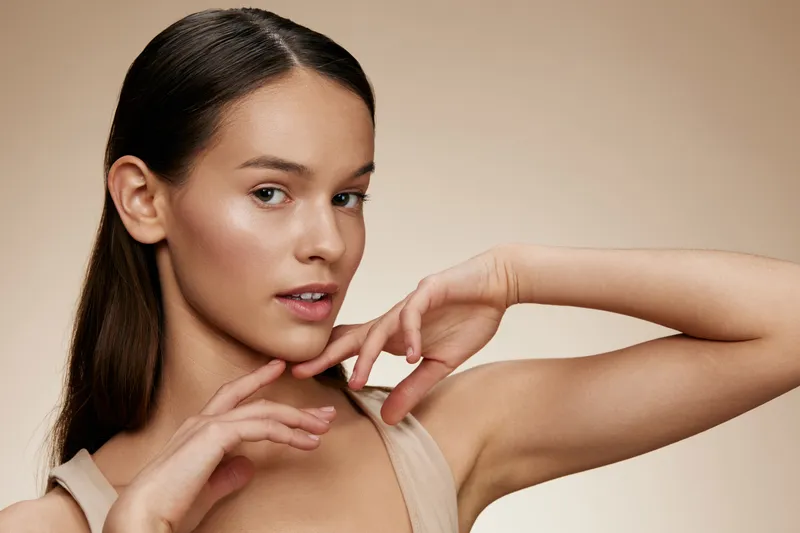 Young female model with smooth skin showcasing natural beauty and elegance, wearing minimal makeup against a soft beige backdrop Perfect for beauty and skincare themes