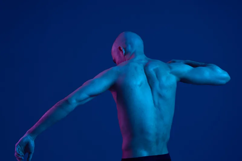 A captivating image of a man posing with a muscular back, exhibiting strength and resilience. The striking monochrome lighting emphasizes the contours of his physique.