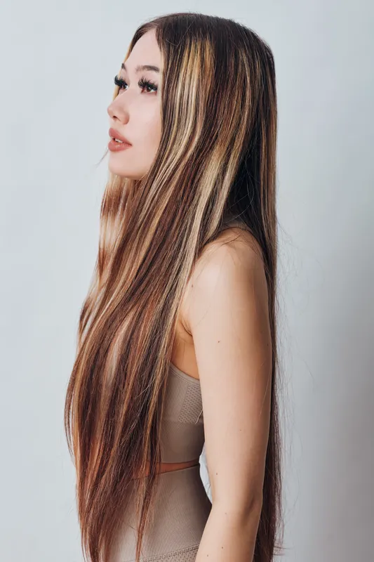 Woman with long straight hair in profile wearing sleeveless top looking forward with soft expression on white background. Beauty, fashion and healthy hair concept.