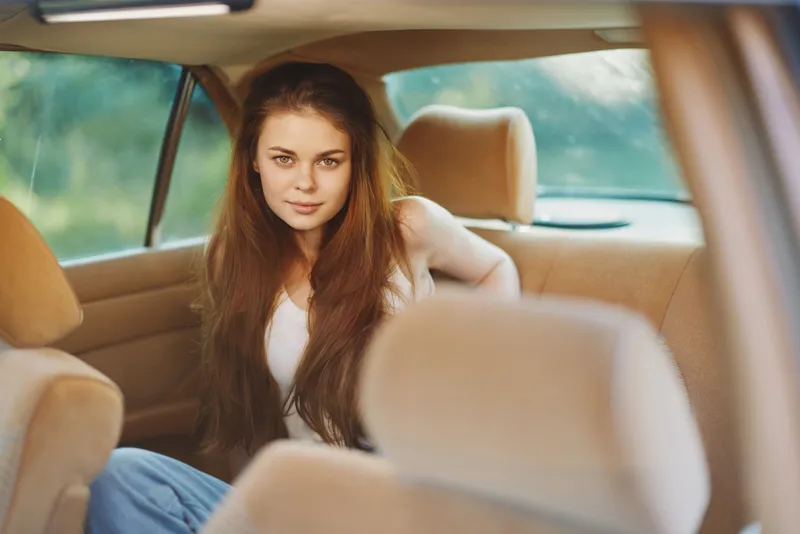 Young woman with long hair sitting in a car, expressing confidence and relaxation, wearing casual clothes, surrounded by a soft, warm-toned interior.