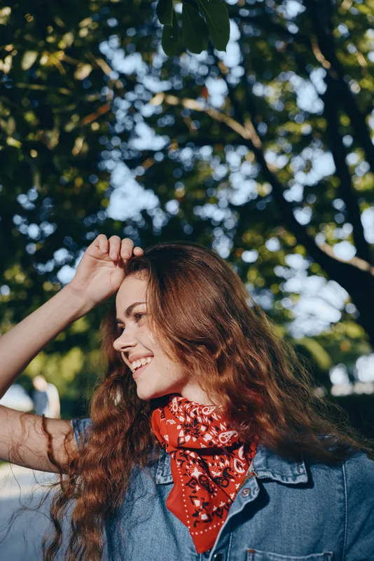 Lifestyle woman wearing red bandana and denim jacket enjoys sunny outdoor moment, modern boho-western denim street style with natural film color tones.