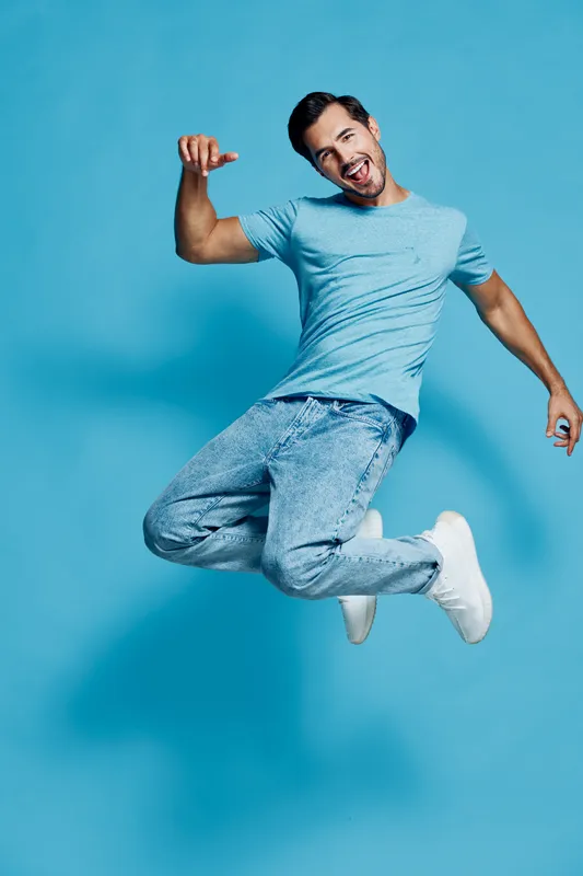 Full body joyful happy energetic young man in light blue t-shirt jumps in the air with excitement, isolated on vibrant solid blue background. People lifestyle concept.