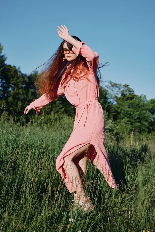 Young woman in a pink dress joyfully dancing in a sunny meadow, showcasing emotion and connection with nature in a vibrant setting