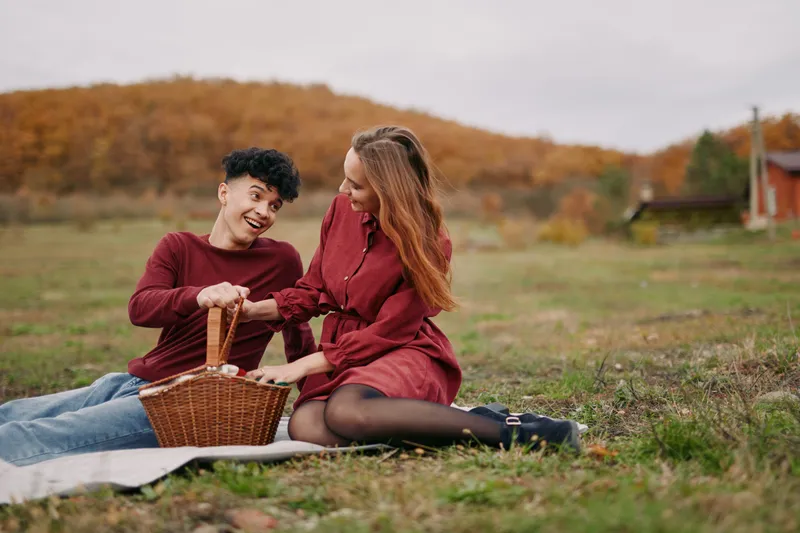 Young couple sharing a candid picnic moment in an autumn meadow, natural gestures and warm smiles evoking authenticity and trustworthiness, relaxed wardrobe and honest interaction.