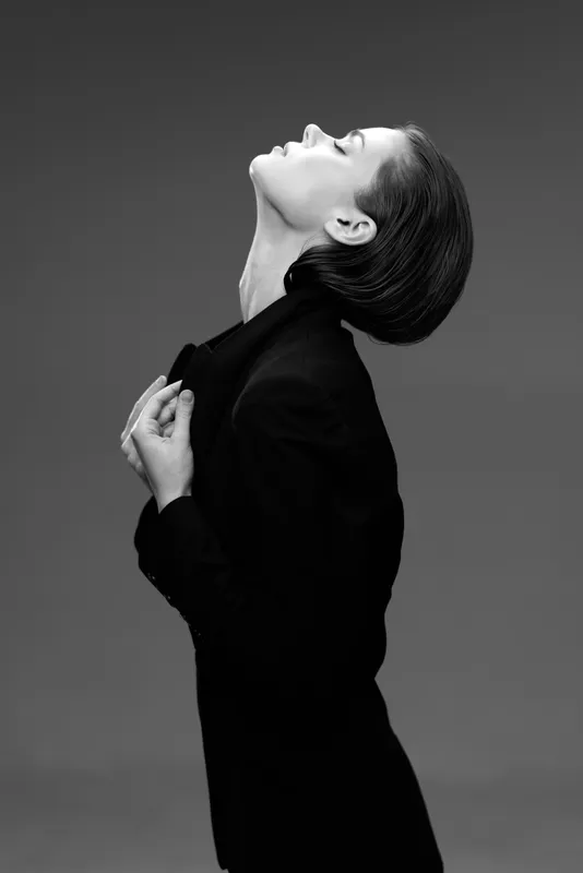 Black and white portrait of elegant woman in turtleneck with stylish hairstyle looking upwards in studio.