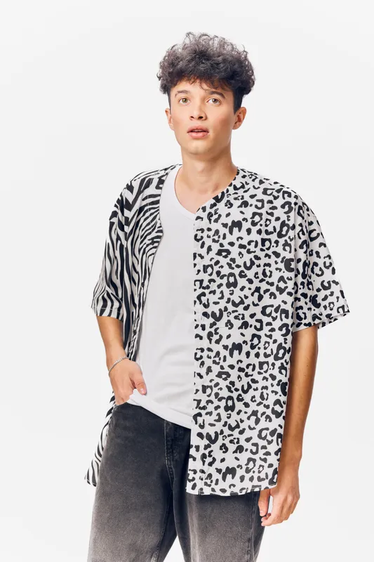 Young man wearing half zebra and half leopard print shirt with white t-shirt and dark jeans standing against white background with surprised facial expression.