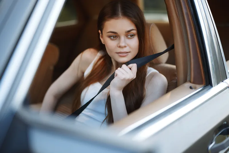 Beautiful young woman relaxing in the car, wearing a casual white tank top, with a thoughtful expression and warm lighting, ideal for travel and adventure themes.