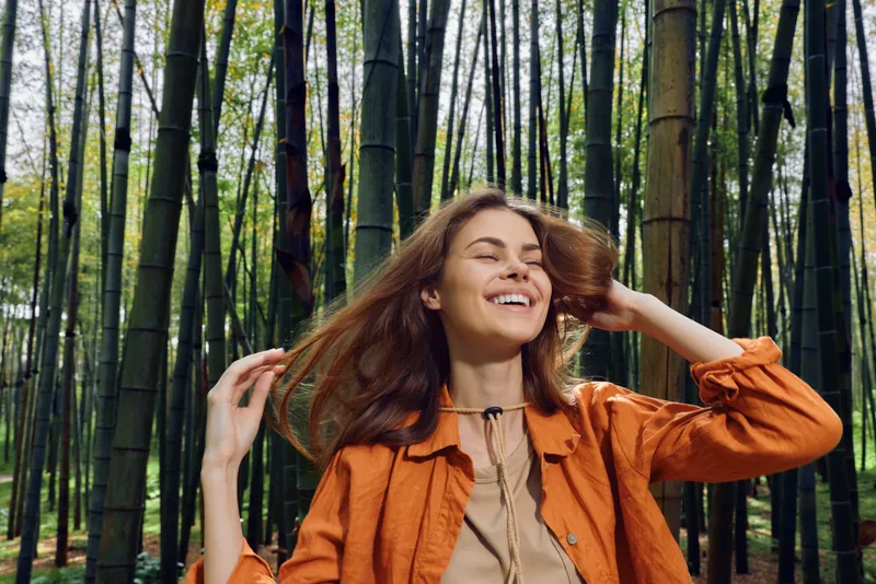 Woman smiling in bamboo forest, portrait of happy young woman outdoors wearing orange jacket, natural light and relaxed expression, nature scene with trees and peaceful mood