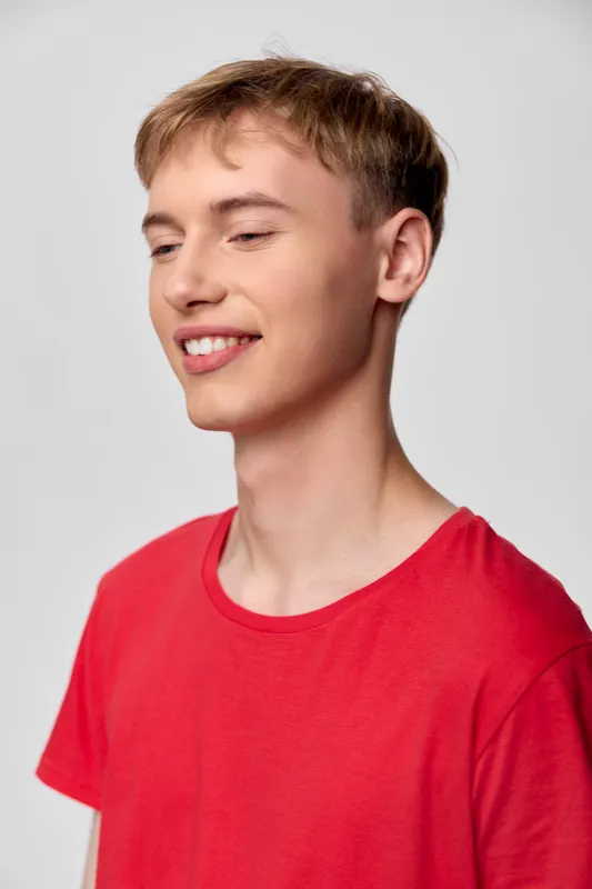 Smiling youth, young man in a red shirt, casual wear, relaxed pose with cheerful expression under studio lighting, showcasing fashion, happiness, and a bright background for lifestyle and