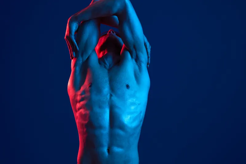Athletic man posing with dynamic lighting, expressing strength and confidence in a striking blue and red color composition, emphasizing his physique and posture.