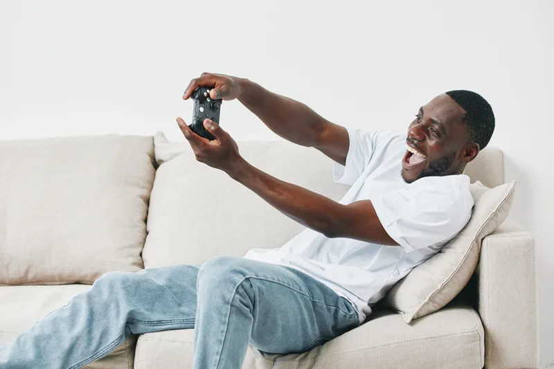 Excited young man enjoying video gaming in casual attire, showcasing vibrant emotions on a cozy sofa in a modern living room setting