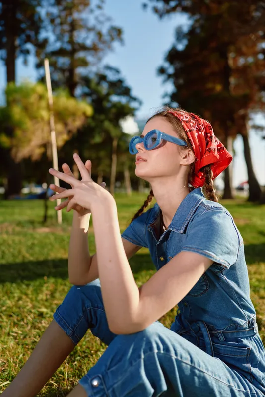 lifestyle woman in modern boho-western denim street style with blue sunglasses and red bandana enjoys sunny outdoor park in film color tones