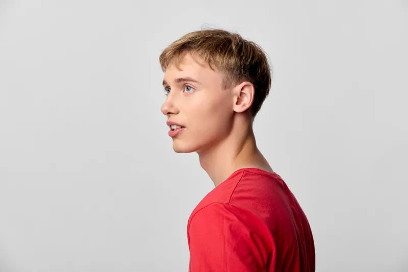 Young man profile side view red shirt in studio shot, casual with calm expression against a clean background, suitable for fashion and lifestyle campaigns