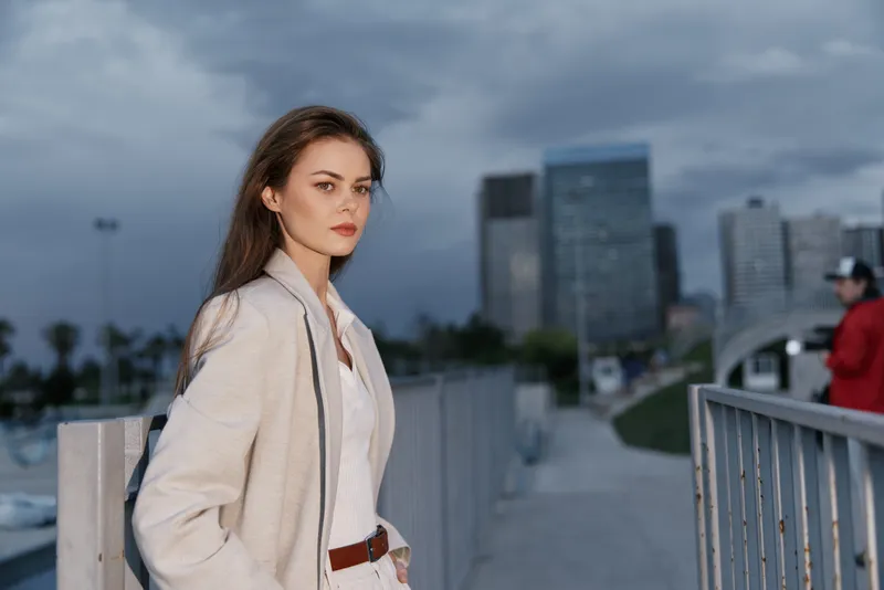 Confident businesswoman standing with a city skyline backdrop, dressed in stylish attire, exuding professionalism and determination.