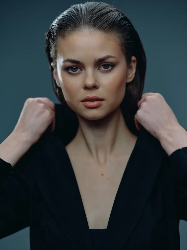Portrait of a confident woman with sleek hair wearing a black blazer against a dark background.