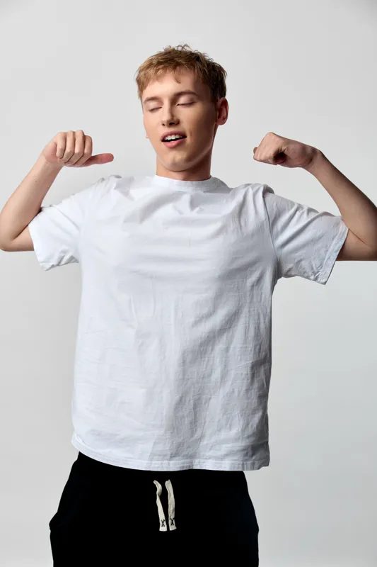 Casual male in white t shirt flexing arms to show confidence and casual strength in a clean studio setting, ideal for lifestyle, fitness or apparel campaigns today.