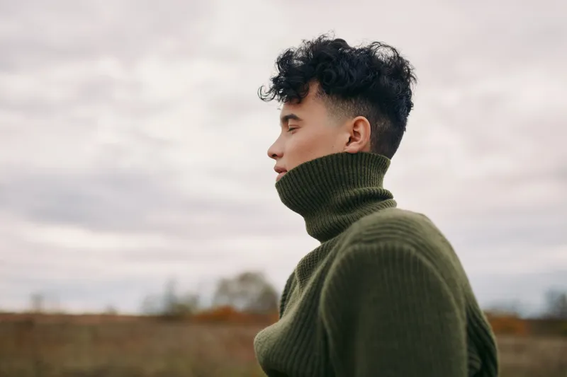 A candid portrait of a young person in a chunky green turtleneck, captured in natural light to emphasize authenticity, truthfulness, and quiet self confidence.