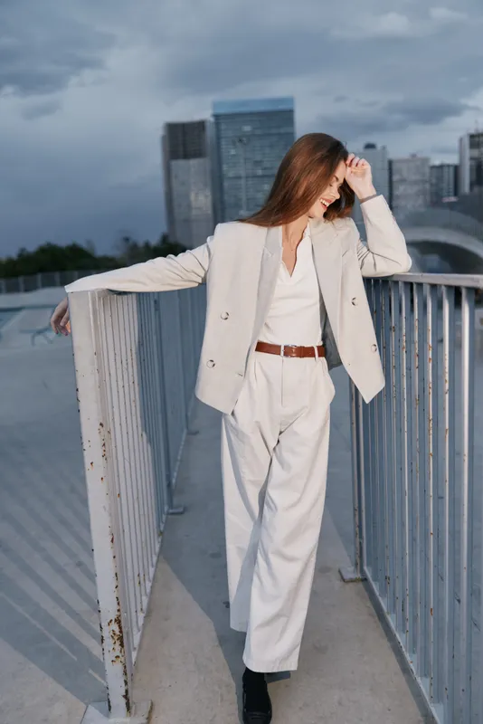Professional woman in a stylish business outfit poses confidently on a rooftop, showcasing a modern urban background with a cool color palette.