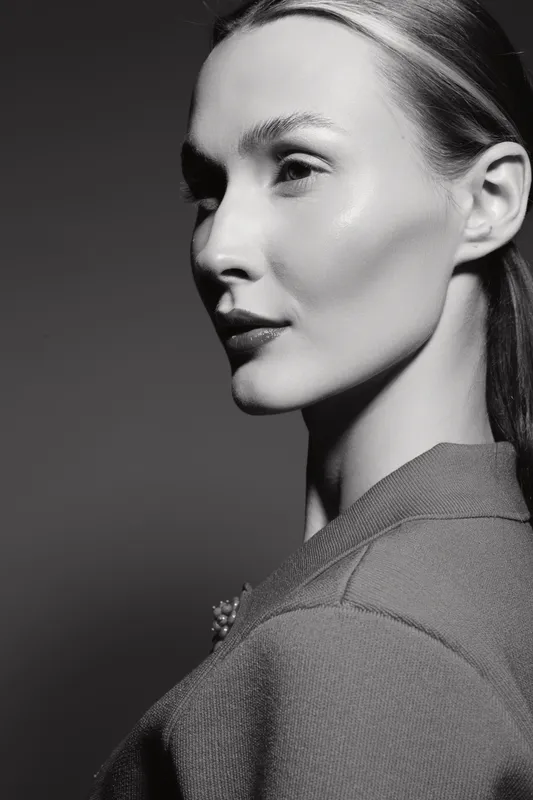 Portrait of a young white woman with fair skin and sleek hair wearing a jacket. Studio lighting highlights her facial features. Beauty and fashion concept.
