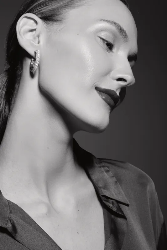 Elegant white woman with light skin and slicked hair posing in profile with earrings in black and white studio portrait.