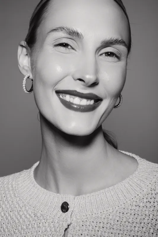 Smiling Caucasian woman with fair skin wearing hoop earrings and knitted sweater. Close-up portrait in black and white with natural expression and soft lighting.