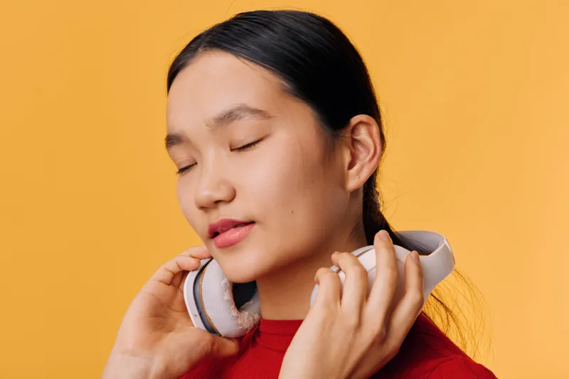 Young woman with closed eyes enjoys music wearing headphones on yellow background. Relaxation, listening, calm expression, casual style, and comfort in leisure time.