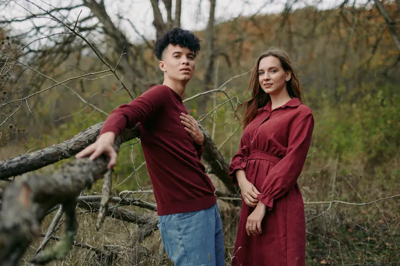 Young couple posing outdoors in an autumn forest scene, relaxed and connected with genuine expressions, conveying authenticity and credibility in a natural candid portrait of relationship.