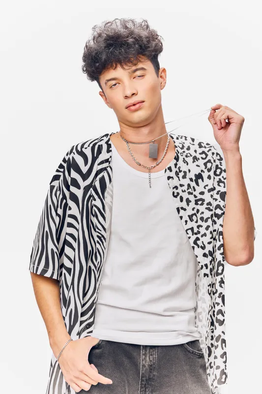 young man wearing stylish mixed animal print shirt with casual white tank top posing confidently against plain white background, modern fashion look