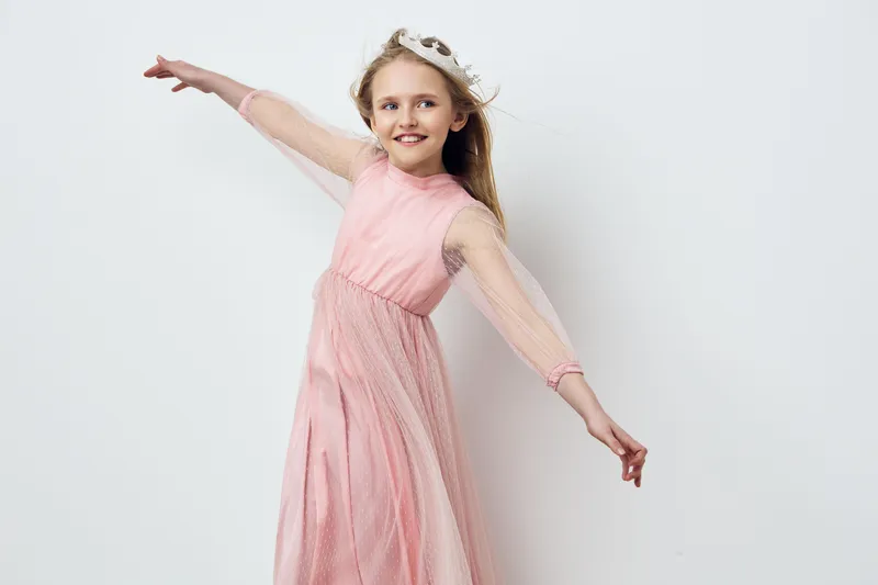 Joyful girl in a pink tulle dress, dancing against a light background, showcasing happiness and innocence, perfect for children s fashion concepts