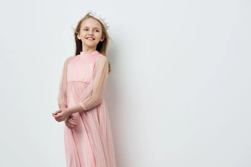 Cheerful young girl in a pink dress with a floral headband, smiling against a soft white background, perfect for seasonal celebrations and children s portraits