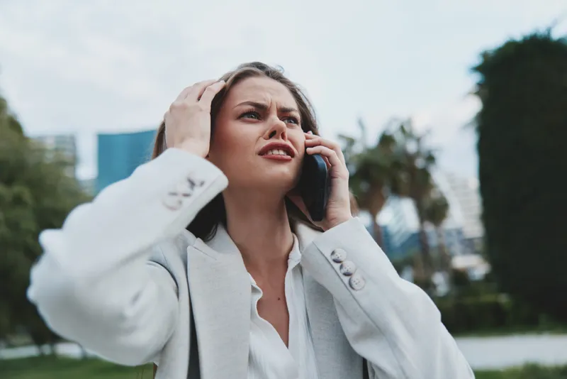 Stressful businesswoman on the phone in a modern outdoor setting, showcasing emotions of worry and frustration while dressed in professional attire.