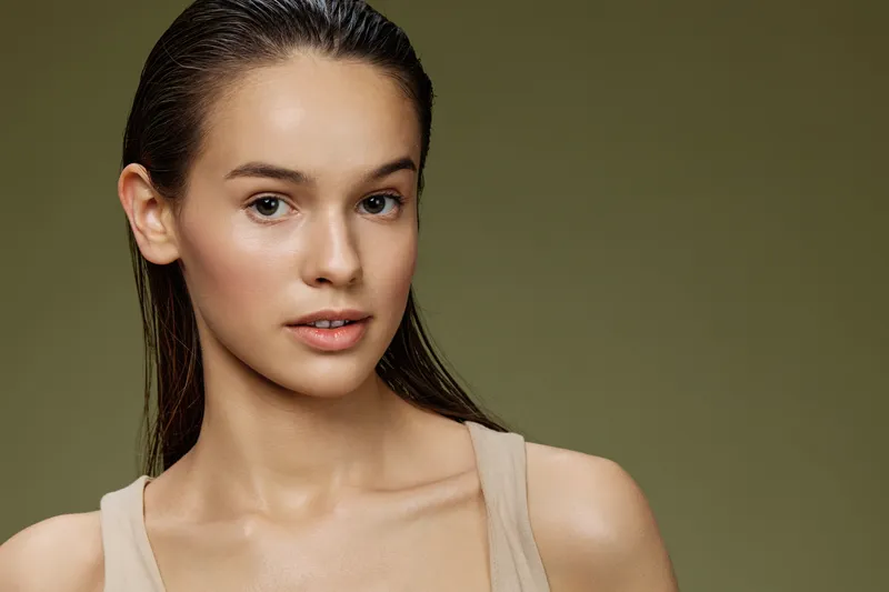Young female model with natural look in neutral clothing, showcasing healthy skin against a soft green background, conveying a sense of calm and serenity